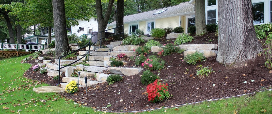 A landscape bed on a hill slope with boulders and mulch installation in Marne, MI.
